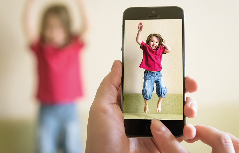 Erwachsene Person die ein Kind mit einem Handy fotografiert