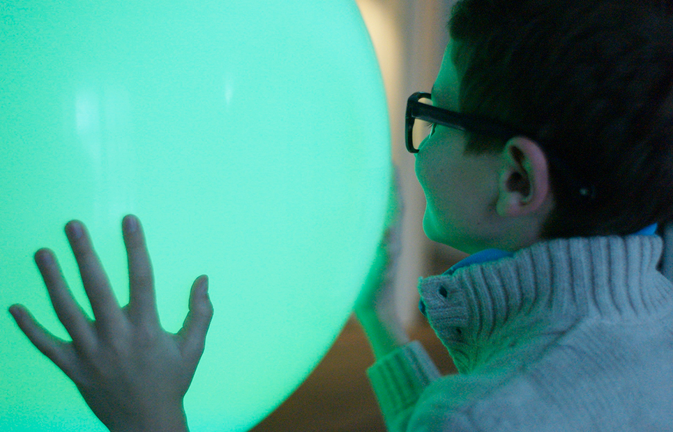 Kind steht vor einer grün leuchtenden Kugel und berührt diese mit seinen Händen