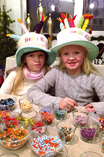 Zwei Mädchen mit Geburtstagshüten vor versch. Schalen mit bunten Perlen