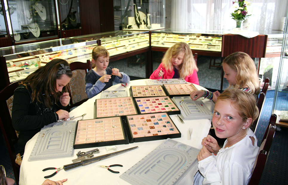 Kinder sitzen zusammen an einem Tisch und gestalten ein individuelles Schmuckstück