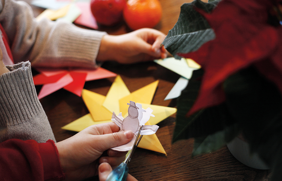 Kinder basteln Weihnachtsdekoration aus Papier. Man sieht nur die Hände, die gerade einen Schneemann ausschneiden