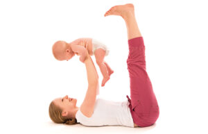 Eine Mama Gymnastik. Sie liegt auf dem Rücken, mit den Beinen in die Luft. Sie hält ihr Baby ebenfalls in die Luft.