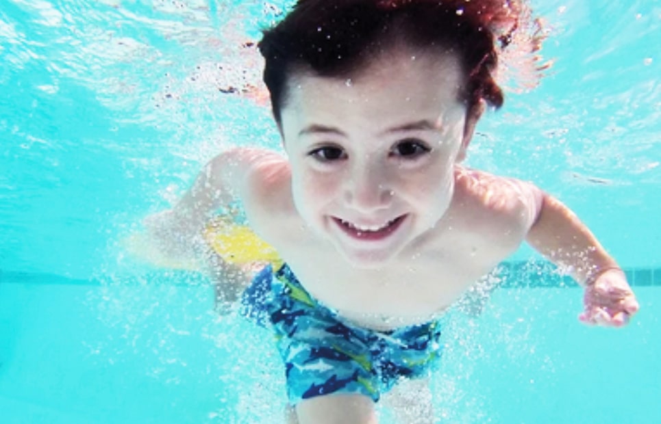 Ein Kind taucht und schaut unter Wasser in die Kamera