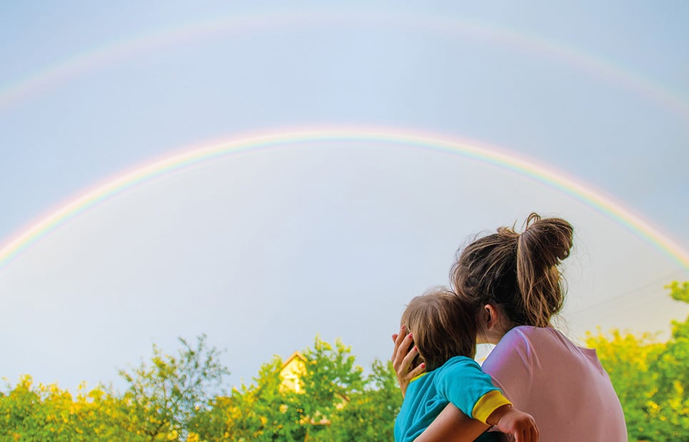 Mama mit Kind schaut einen Regenbogen an